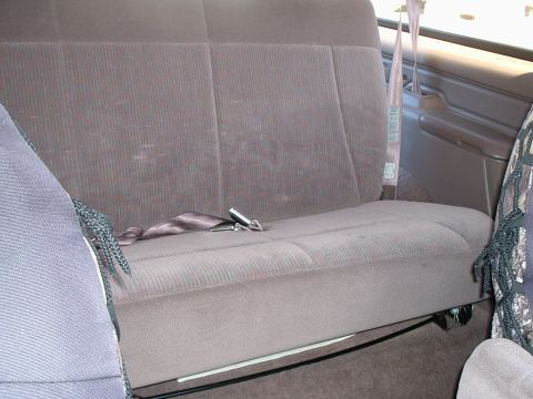 1996 Ford Bronco - Gray ribbed cloth rear bench seat with folded seat belts inside a truck or SUV cabin.