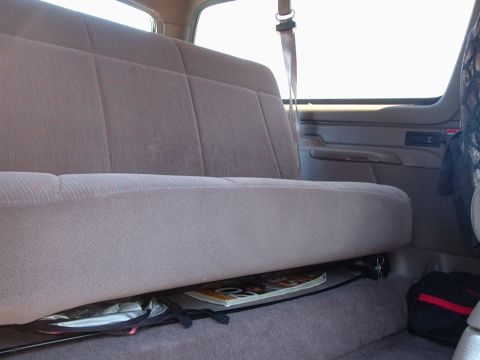 1996 Ford Bronco - Interior shot of a tan cloth rear bench seat in a two-door truck-based SUV, with the shoulder belt hanging from the B-pillar and a molded t…