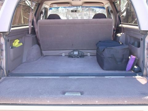 1996 Ford Bronco - Rear cargo bay of an SUV with the second-row seats folded down, showing carpeted floor and a black duffel bag.