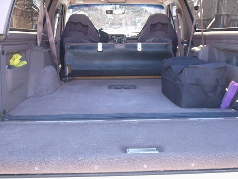 1996 Ford Bronco - Cargo area of a full-size SUV shot through the open tailgate with the rear bench folded flat, showing tan carpeted floor and lowered tailga…