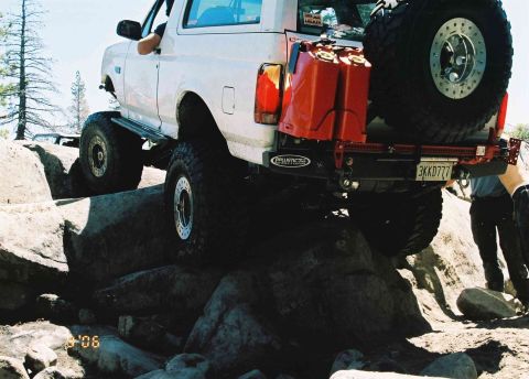 1995 Ford Bronco - This SUV is tackling a challenging off-road course with large rocks and uneven terrain.