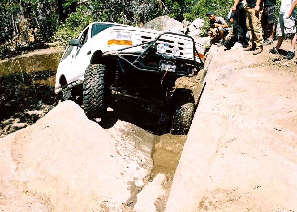 White Ford 4x4 truck crawling through a rocky rut on a trail