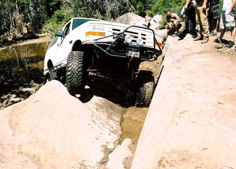 1995 Ford Bronco - This modified truck is navigating a challenging off-road obstacle with spectators observing the action.