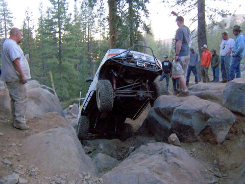 1995 Ford Bronco - Off-road vehicle struggles on a steep rock obstacle with spectators watching.