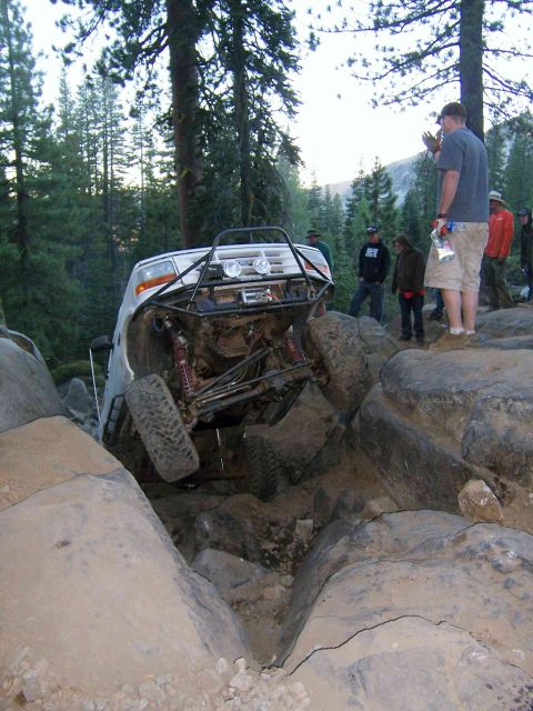 1995 Ford Bronco - This modified SUV is navigating a difficult rocky terrain, with onlookers observing the challenging maneuver.