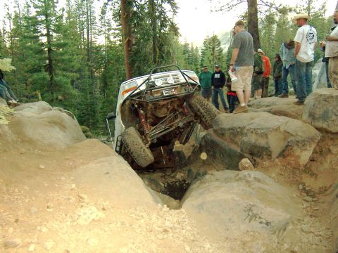 1995 Ford Bronco - An off-road SUV is stuck on its side between large rocks on a challenging trail.