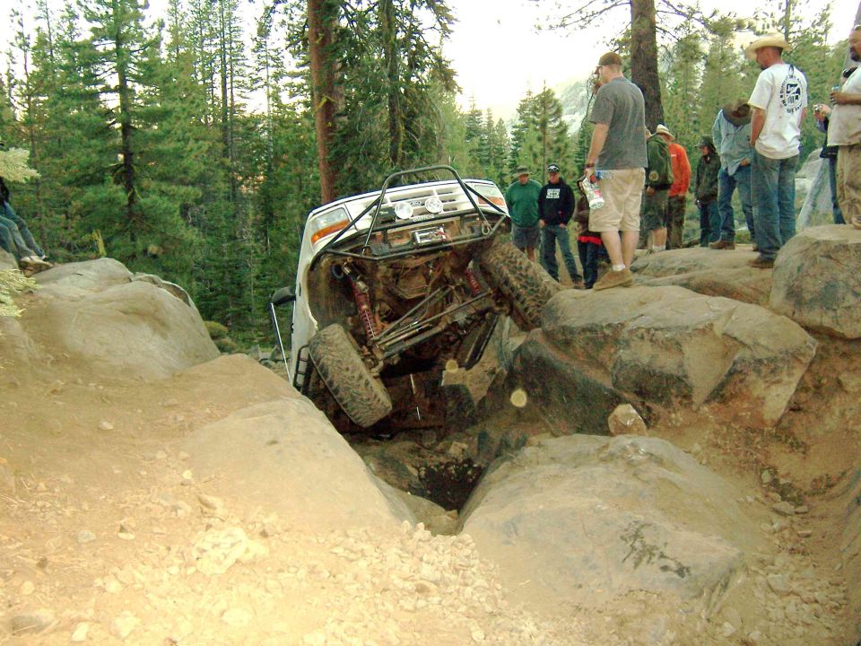 White off-road SUV tilted on its side, stuck between large rocks on a dirt trail