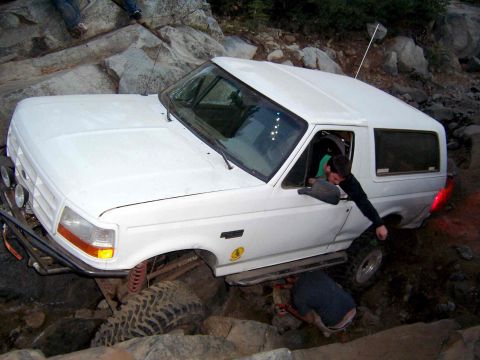 1995 Ford Bronco - A white 1995 Ford Bronco is navigating a difficult rocky terrain, with assistance from individuals outside the vehicle.