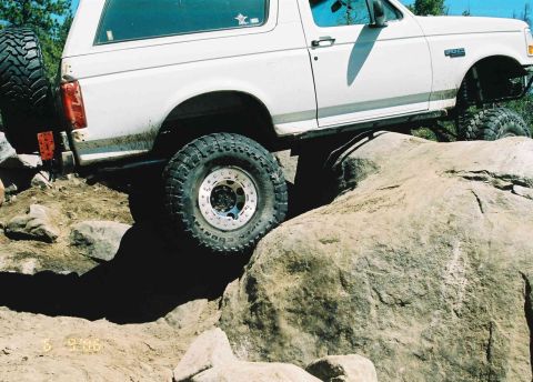 1995 Ford Bronco - This white Ford Bronco is navigating a rocky trail, showing off its off-road modifications.