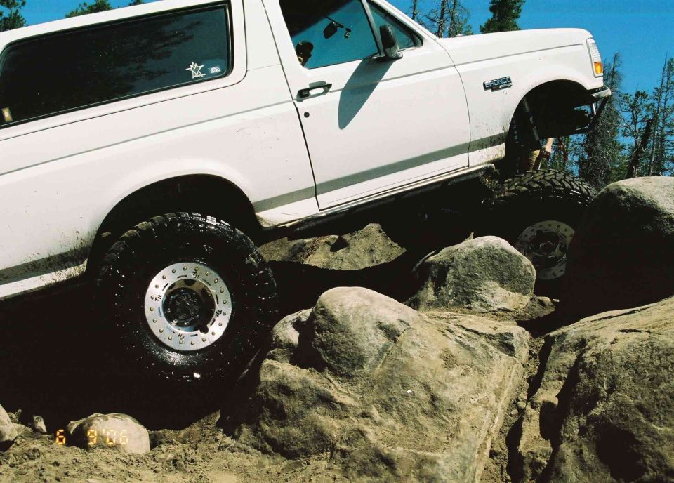 White 1992 Ford Bronco with off-road tires navigating large rocks