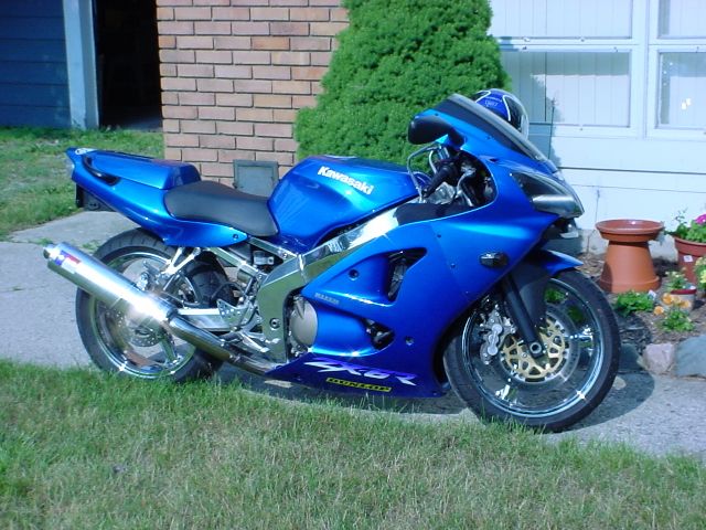 Blue Kawasaki sportbike parked on grass in front of a brick building and a window