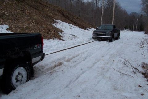 2000 Chevrolet Tahoe - A black pickup truck is being towed through a snowy landscape by another truck.