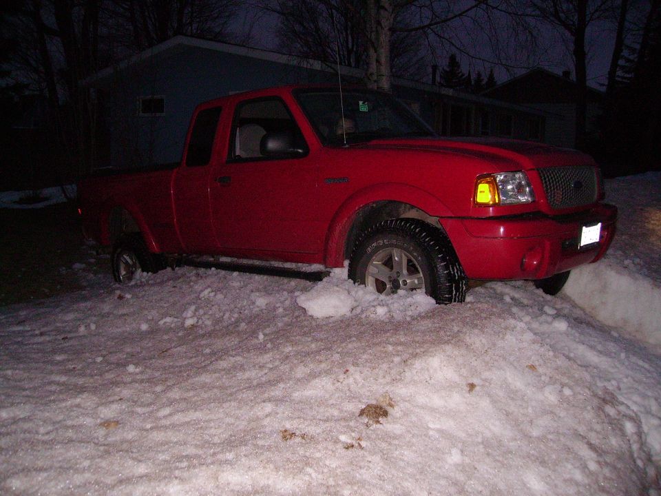 Red Ford Ranger pickup truck with front wheels stuck in a snowdrift