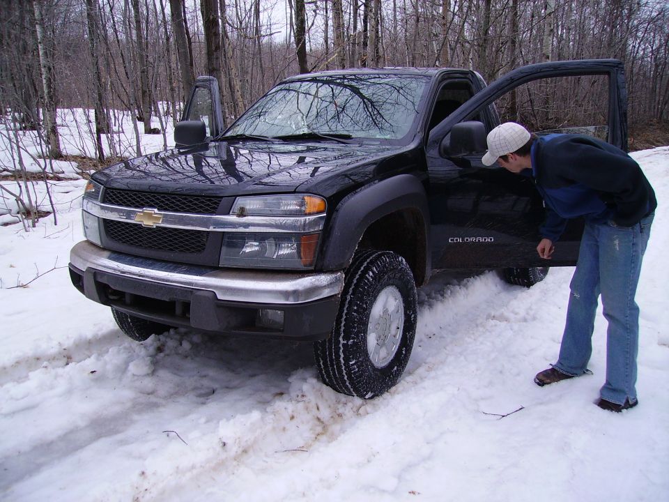 Black Chevrolet Colorado pickup truck with doors open in snow, person looking inside