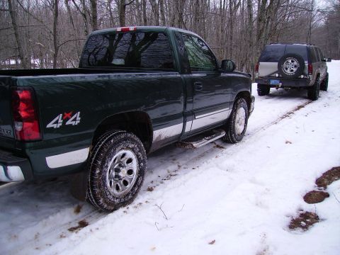 2000 Chevrolet Tahoe - A green pickup truck and an SUV are parked on a snowy road in a wooded area.