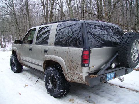 2000 Chevrolet Tahoe - Rear view of a lifted 2000 Chevrolet Tahoe with a spare tire mounted on a custom bumper, driving in the snow.