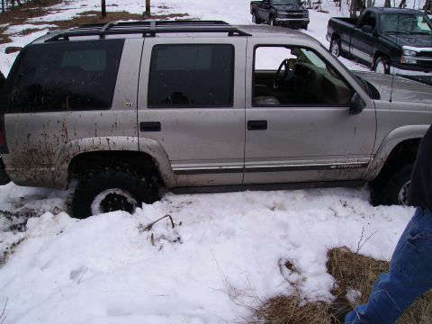 2000 Chevrolet Tahoe - A silver SUV is stuck in deep snow, with two pickup trucks in the background.