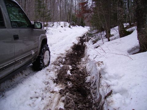 2000 Chevrolet Tahoe - A silver SUV navigates a challenging snowy path with deep ruts and surrounding trees.