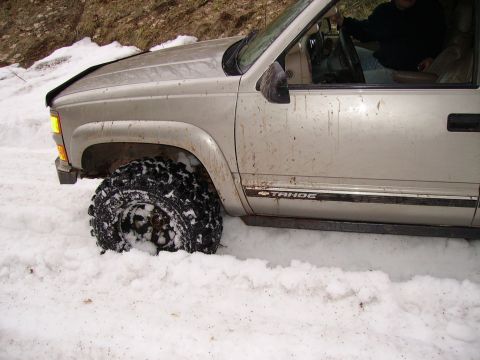 2000 Chevrolet Tahoe - This silver SUV, identified by its "TAHOE" badge, is stuck deep in the snow, with only its front wheel visible.