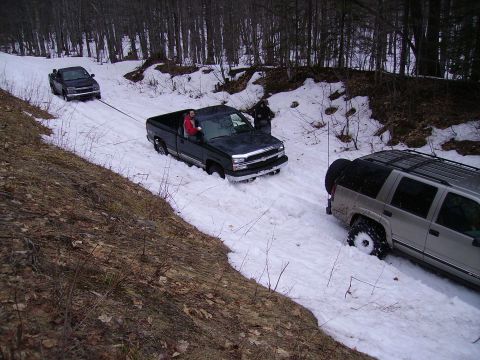 2000 Chevrolet Tahoe - Three vehicles are stuck in the snow on a wooded road, with one truck being towed.