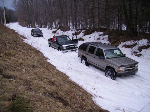 2000 Chevrolet Tahoe - Two trucks and an SUV are stuck in the snow on a wooded road, with one truck towing another.