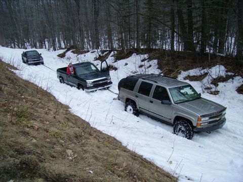 2000 Chevrolet Tahoe - Three vehicles are stuck in the snow on a wooded road, with one being towed.