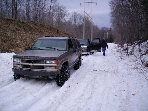 2000 Chevrolet Tahoe - Two SUVs are stuck in the snow on a wooded road with power lines overhead.