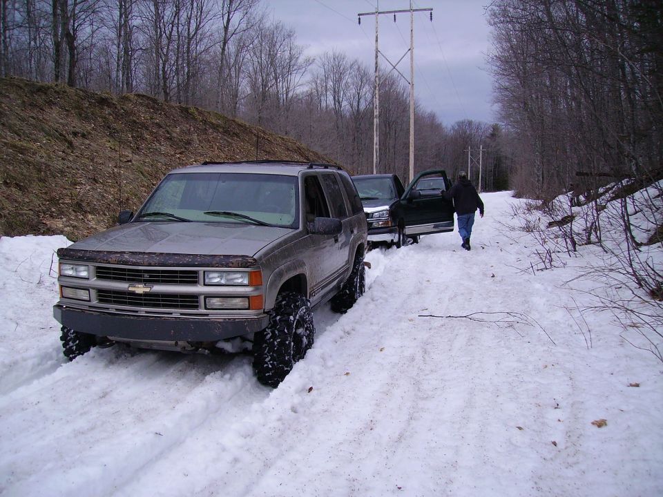 Silver SUV with big tires in snow, another SUV behind it with door open, person walking away