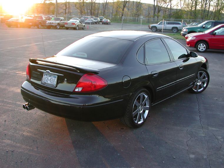 Black four-door sedan, three-quarter rear view, on chrome multi-spoke wheels at sunset
