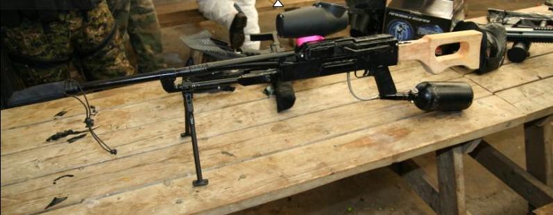 Paintball marker with bipod, scope, and air tank on a wooden table