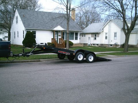 2001 Dodge 2500 - A car hauler trailer is attached to a dark pickup truck, parked on the side of a street in front of houses.