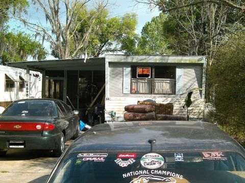 1986 Ford Bronco - Two cars are parked in front of a mobile home with a 'For Sale' sign in the window.