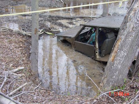 1995 Dodge 1500 - A truck is submerged in mud and water, with its interior visible and a driver seated inside.