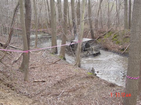 1995 Dodge 1500 - An off-road vehicle is submerged in a muddy creek, with caution tape marking the area.