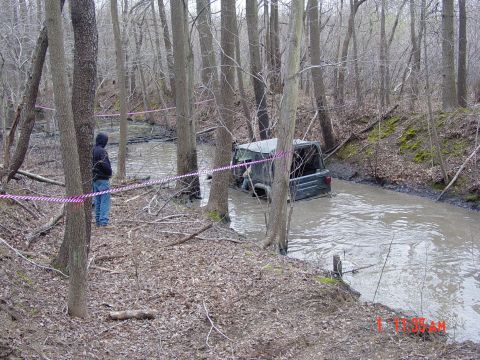 1995 Dodge 1500 - A Jeep Wrangler is stuck in a muddy creek bed, with a person watching from the bank.