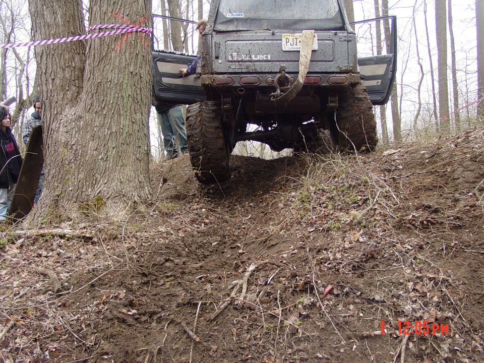 Suzuki Samurai with doors open, stuck on a muddy hill next to a tree
