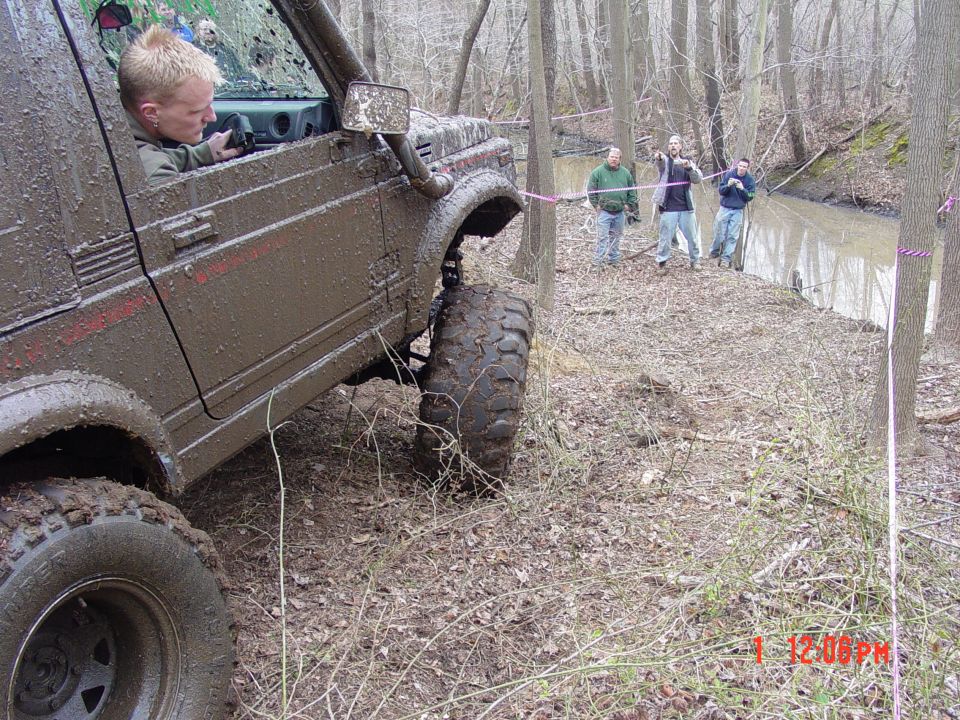 Mud-covered Suzuki Samurai off-roading with a driver inside, tires deep in mud
