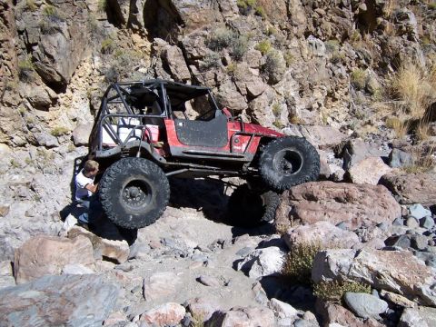 1986 Ford Bronco - A heavily modified off-road vehicle tackles a challenging rocky trail, with a person attending to the front tire.