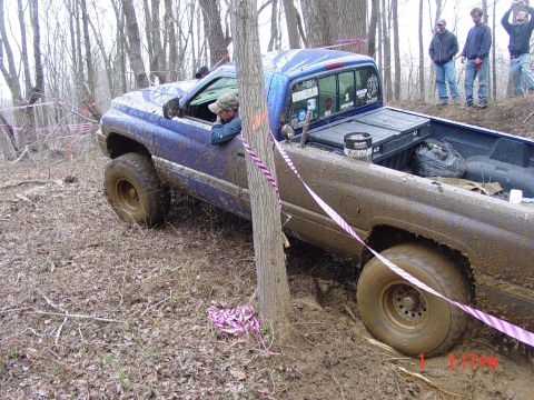 1995 Dodge 1500 - A blue pickup truck navigates a muddy, wooded off-road course, with spectators watching from a rise.