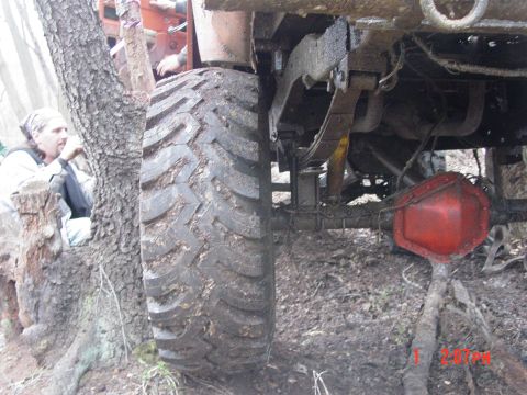 1995 Dodge 1500 - Undercarriage view of a muddy truck with a large tire pressed against a tree.
