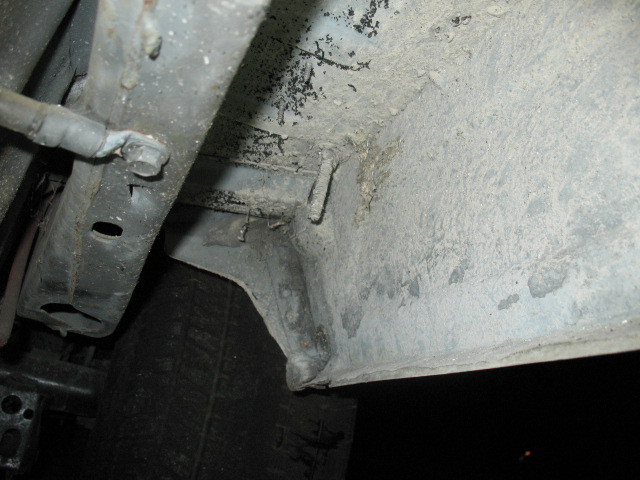 Undercarriage of a vehicle showing frame rails and suspension components, covered in dirt and grime