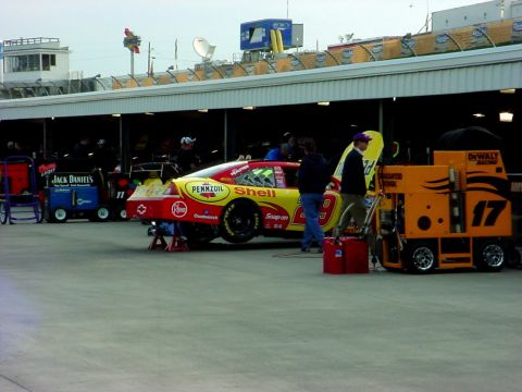 1993 Ford Mustang - A race car is serviced in the pit lane, with various equipment and personnel around it.