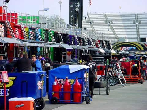 1993 Ford Mustang - Pit lane scene at a NASCAR event, showing garages, crew, and support equipment.