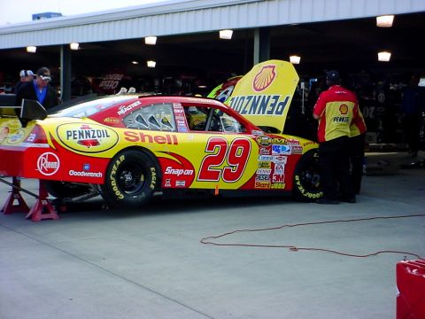 1993 Ford Mustang - A race car with sponsor decals is being worked on in a garage with its hood open.