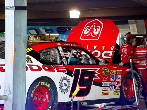 1993 Ford Mustang - A race car with the number 19 and Dodge branding is parked in a garage with its hood open.