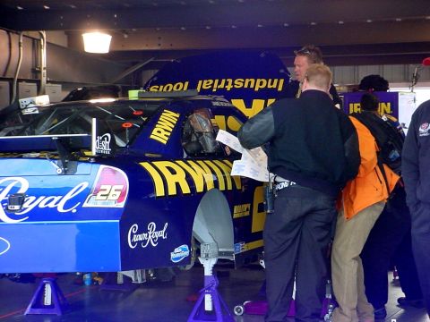 1993 Ford Mustang - A race car is being worked on in a garage, with several people gathered around it.