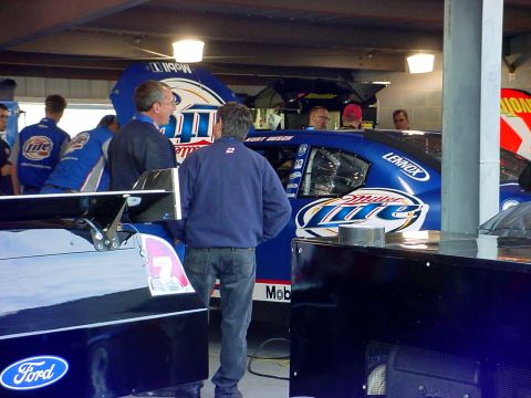 1993 Ford Mustang - Race cars are prepared in a garage, with crew members observing the vehicles.