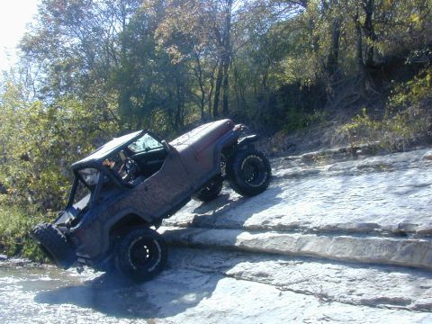 1996 Ford Bronco - An off-road vehicle navigates a rocky terrain with water nearby.