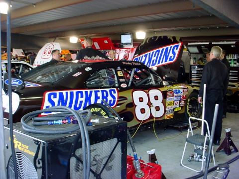1993 Ford Mustang - A race car with Snickers branding is worked on in a garage pit area.