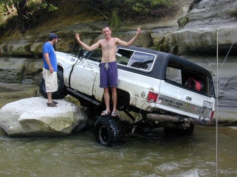 1996 Ford Bronco - Two men pose with a lifted white SUV with a black top as it navigates through shallow water and rocks.